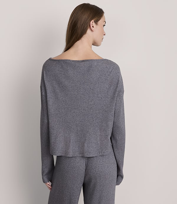A woman in a grey ribbed sweater and pants stands against a plain grey background.