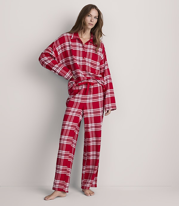 A woman stands in red plaid pajamas against a plain, light-colored background.