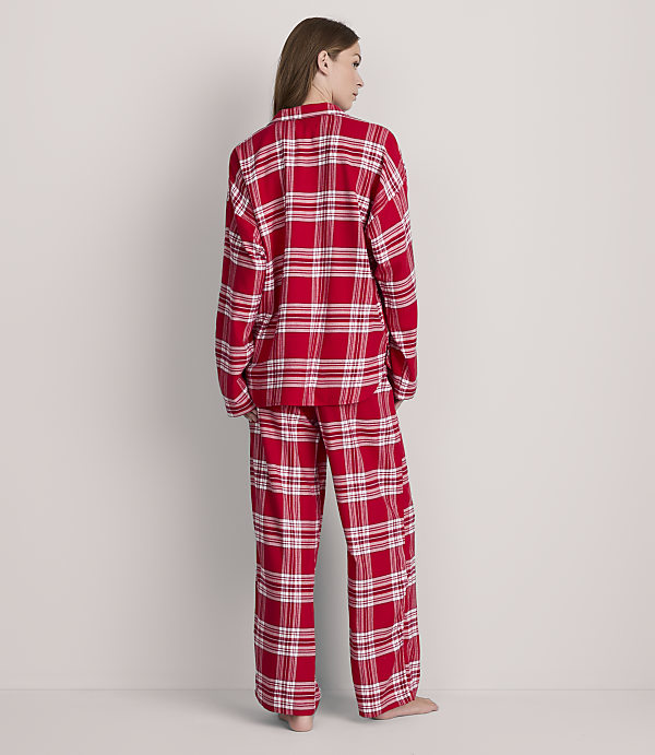 A woman in red plaid pajamas stands against a plain, light gray background.