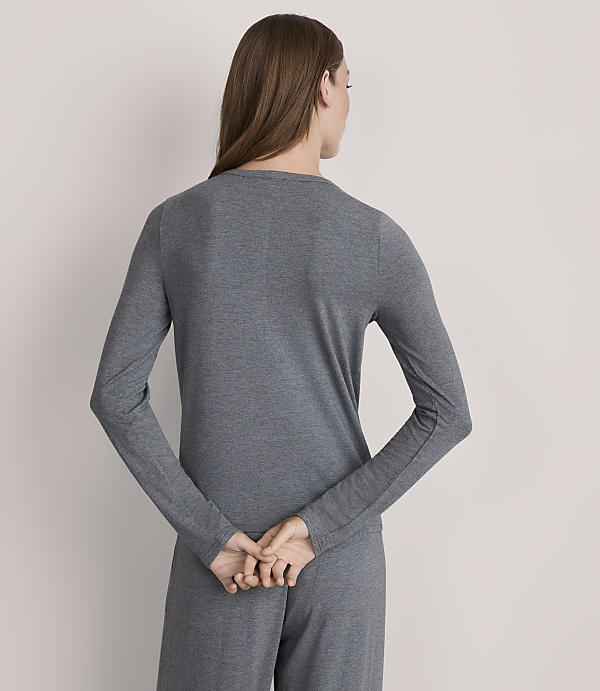 A woman in a grey long-sleeved shirt and pants stands with her back to the viewer against a plain grey background.