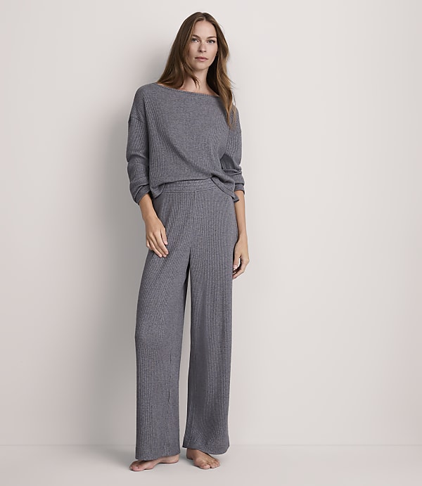 A woman stands in a grey ribbed loungewear set against a plain, light grey background.