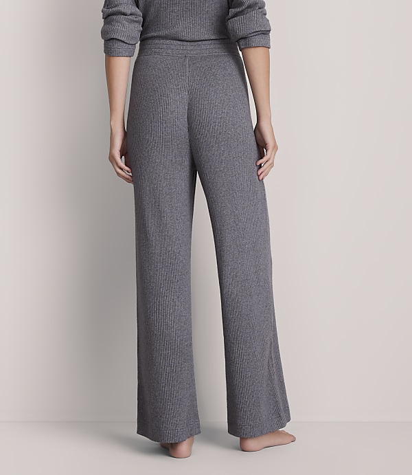 A person wearing grey ribbed pajama pants stands against a plain grey background.