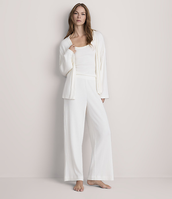 A woman in white pajamas stands against a plain, light-colored wall.