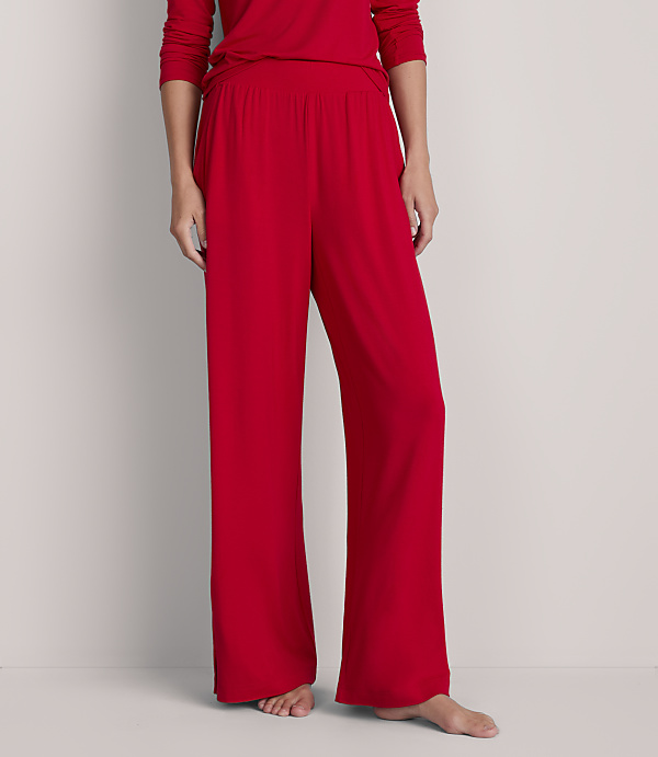 A person stands in red pajama pants and a matching top against a plain, light gray background.