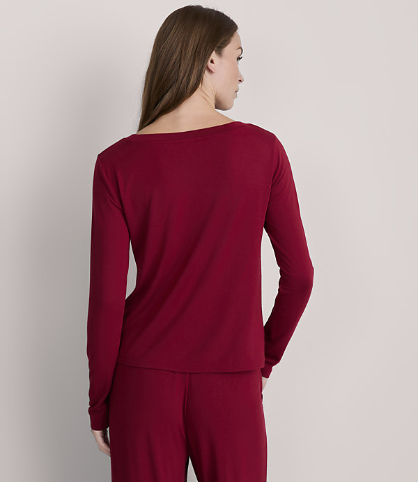 A woman in a maroon long-sleeved shirt and pants stands against a plain gray background.