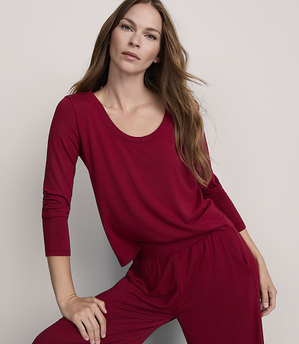 A woman in a maroon pajama set poses against a plain gray background.
