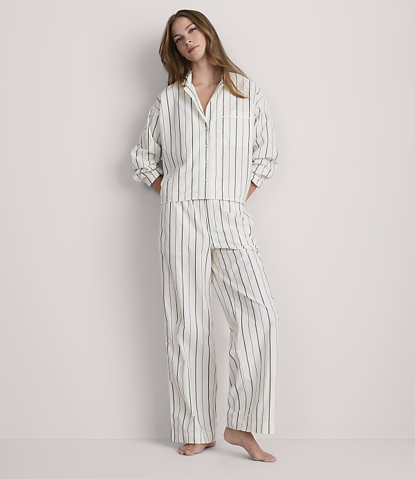 A woman in striped pajamas stands against a plain, light-colored wall.