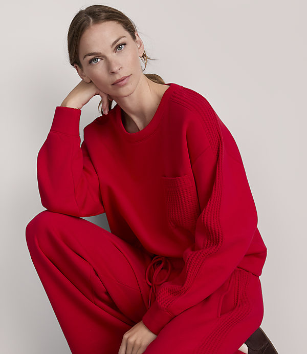 A woman in a red sweater and pants poses against a plain gray background.