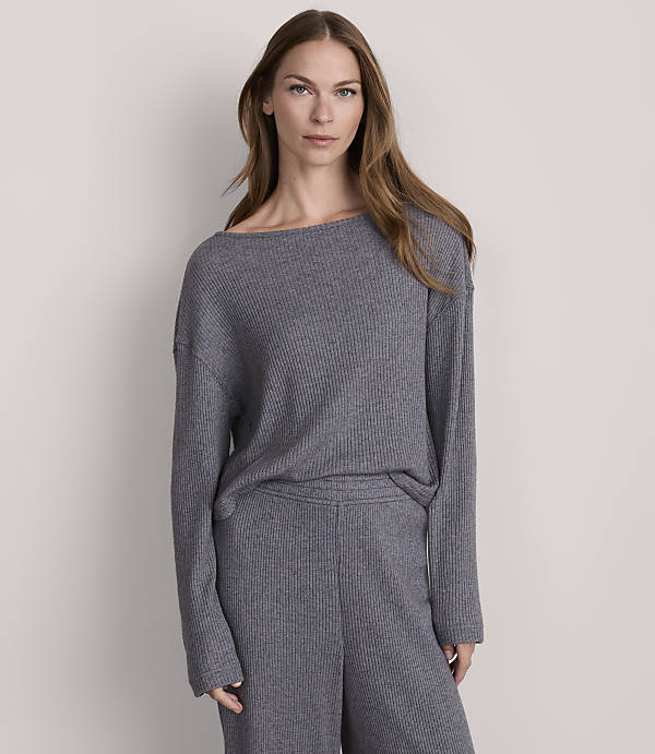A woman in a grey ribbed sweater and pants stands against a plain grey background.