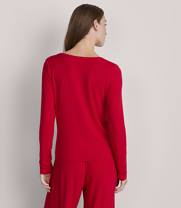 A woman in a red long-sleeved shirt and pants stands against a plain gray background.