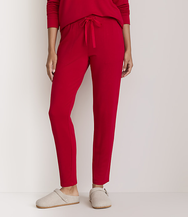 A person wearing red pajama pants and beige slippers stands against a plain white background.