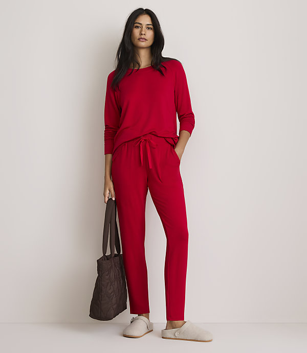 A woman in red pajamas stands with a brown tote bag and slippers against a plain white background.