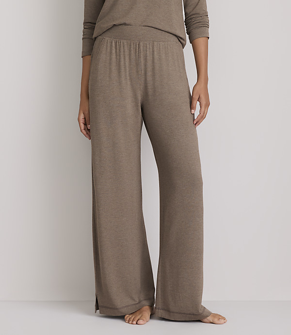 A person stands in loose-fitting brown lounge pants and a matching top against a plain white background.