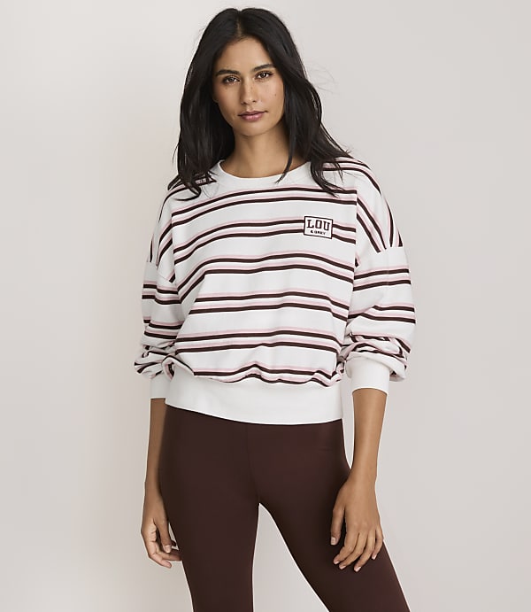 A woman in a striped sweatshirt and brown leggings stands against a plain, light-colored background.