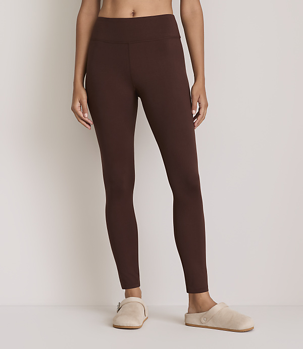 A person wearing brown leggings and light-colored slippers stands against a plain white background.