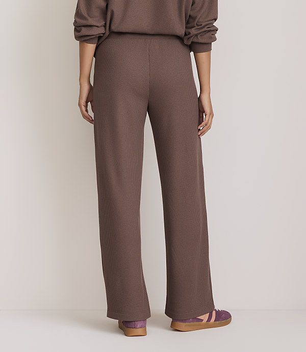 A person wearing brown ribbed pants and purple sneakers stands against a plain, light-colored background.