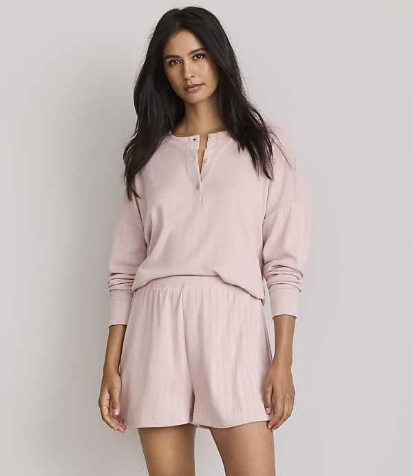 A woman in a pink pajama set stands against a plain gray background.
