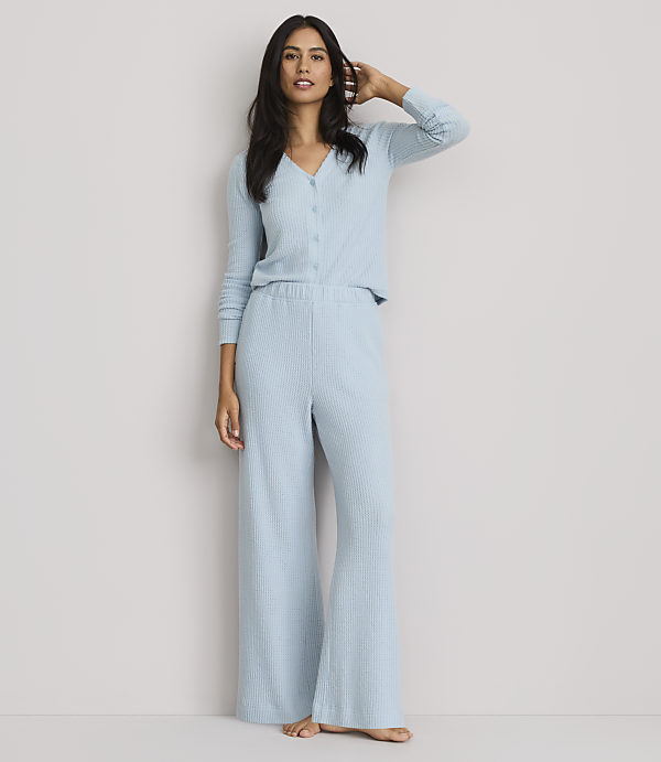 A woman in light blue ribbed pajamas stands against a plain, light gray background.