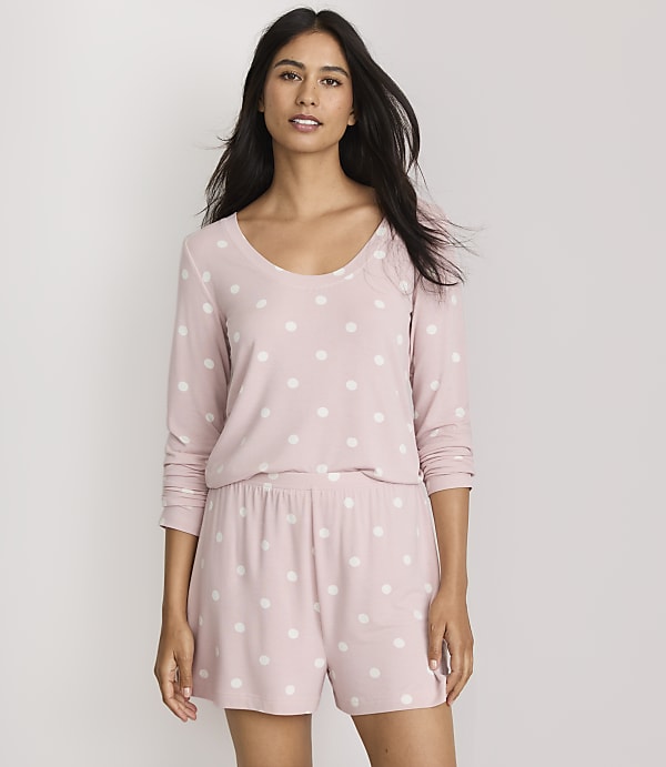 A woman in a pink polka dot pajama set stands against a plain white background.