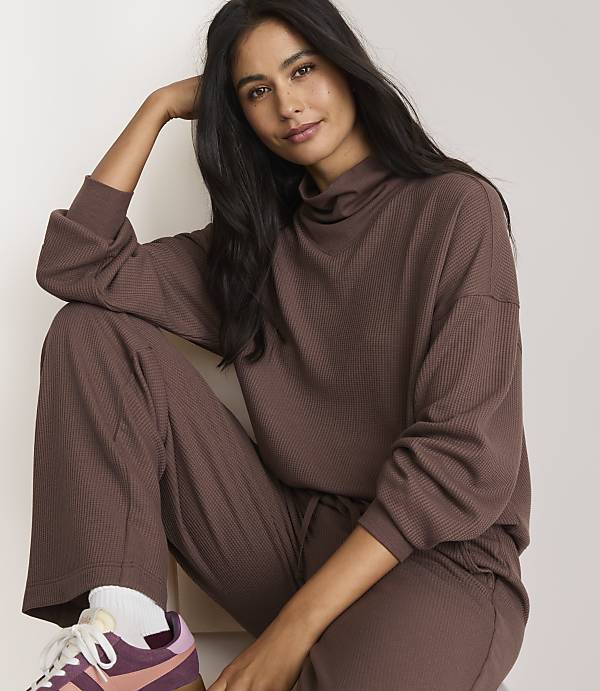 A woman in a brown loungewear set poses against a plain white background.