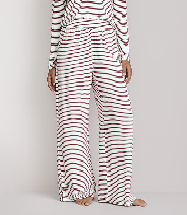 A person stands wearing striped pajama pants and a matching top against a plain white background.
