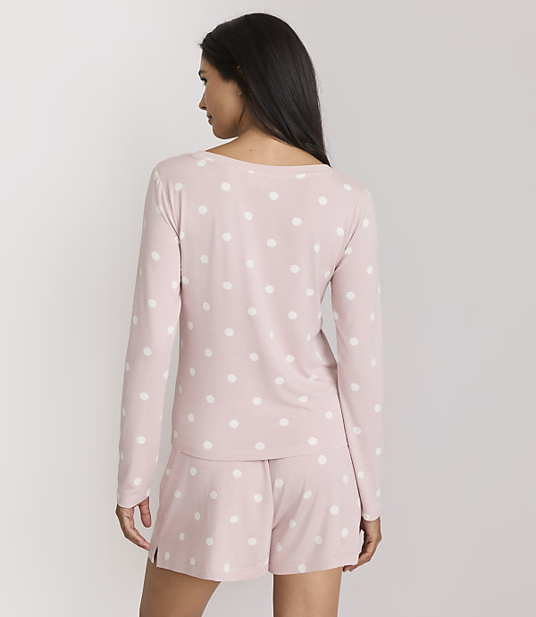 A woman in pink polka dot pajamas stands against a plain white background.