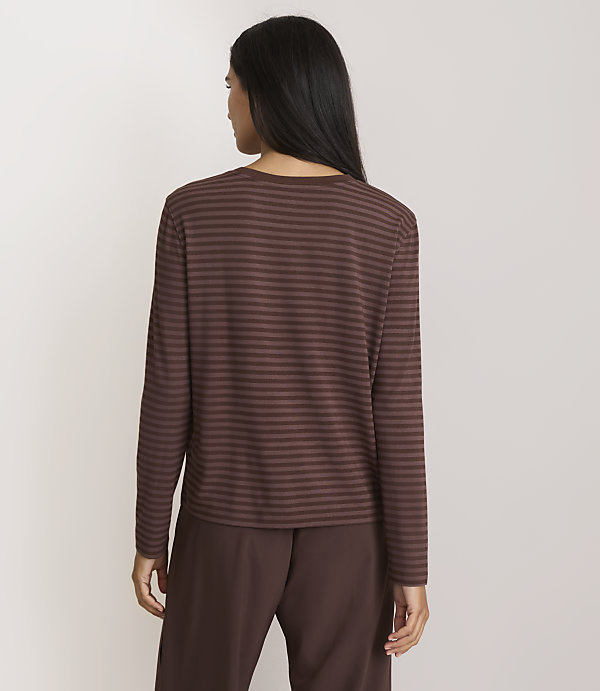 A woman in a brown striped shirt and brown pants stands against a plain, light background.