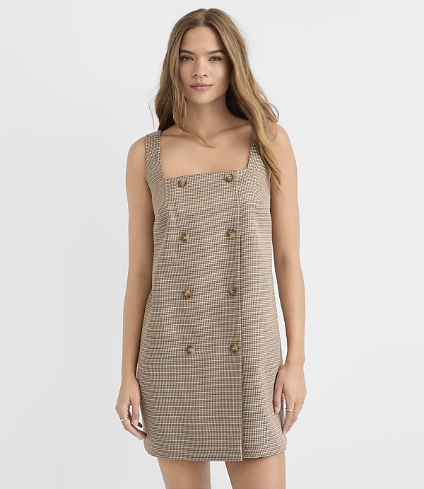 A young woman in a plaid dress stands against a plain white background.
