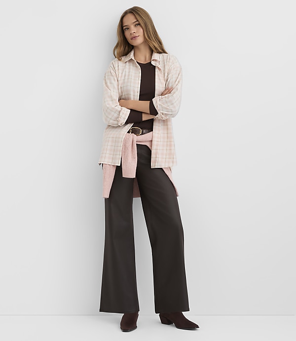 A woman in a plaid shirt and wide-leg pants stands against a plain white background.