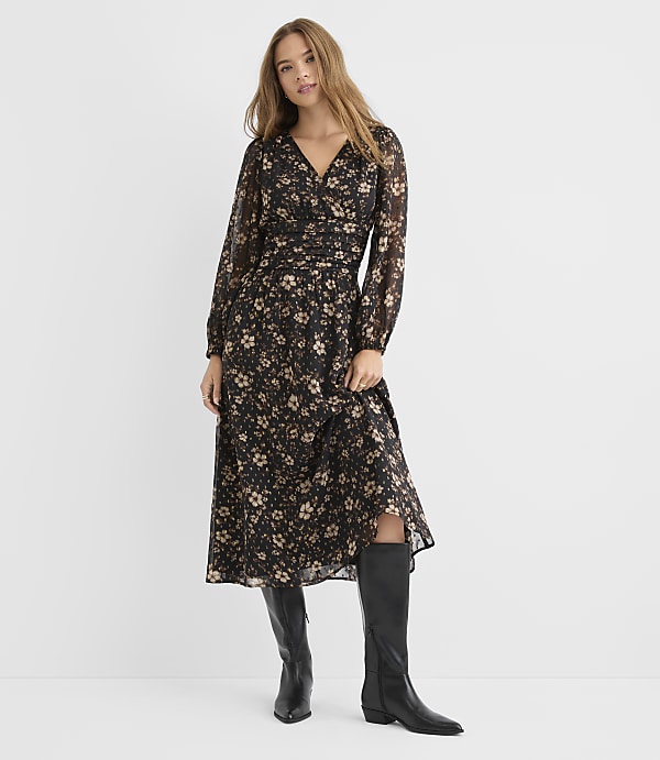 A woman in a floral print dress and black boots stands against a plain white background.