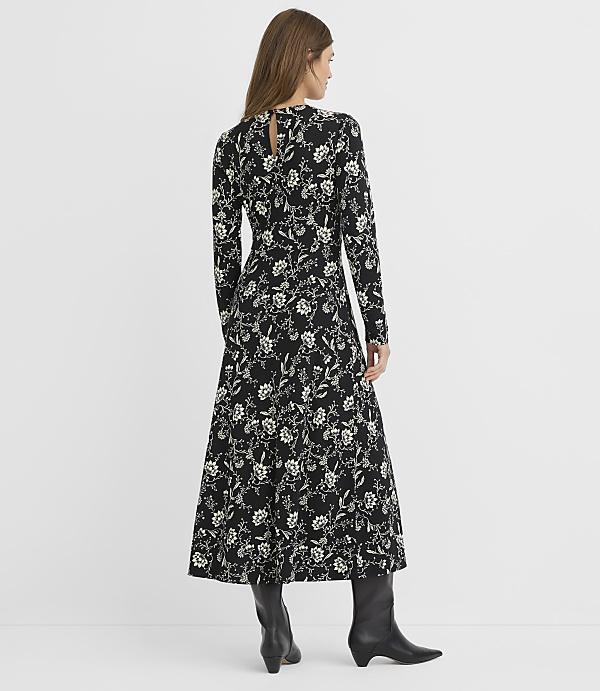 A woman in a black floral dress and black boots stands against a plain white background.