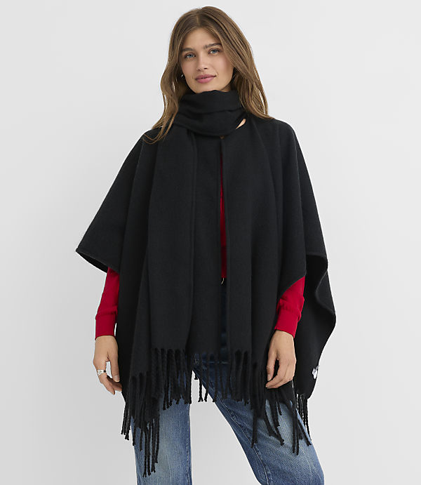 A woman in a black fringed poncho and scarf stands against a plain white background.