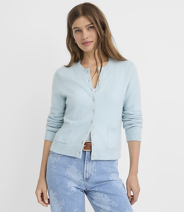 A woman in a light blue cardigan and jeans stands against a plain white background.