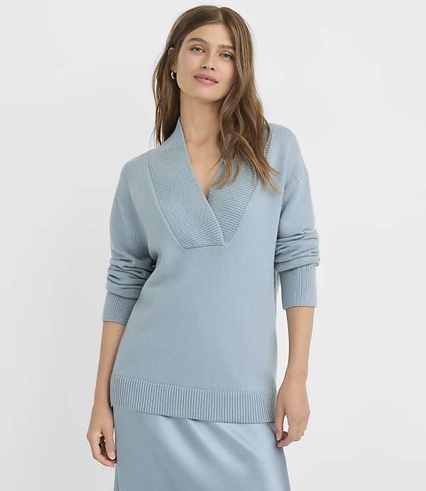 A woman in a light blue V-neck sweater stands against a plain, light blue background.