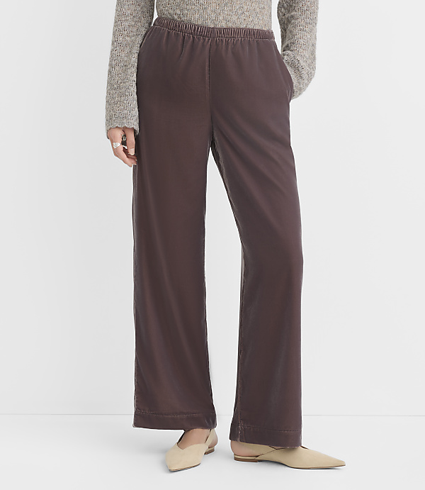 A person wearing brown wide-leg pants and a grey sweater stands on a white background.
