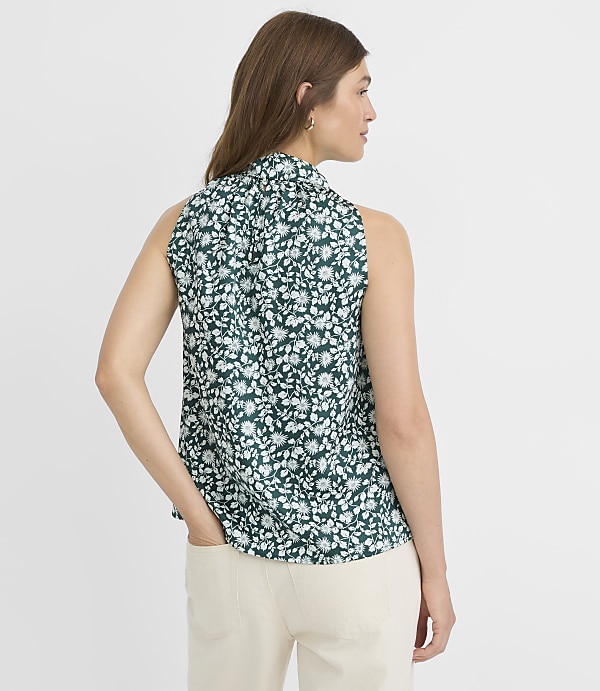 A woman in a floral top and jeans stands against a plain white background.