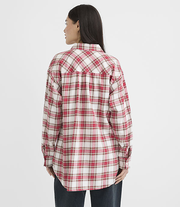 A woman in a red and white plaid shirt stands against a plain white background.