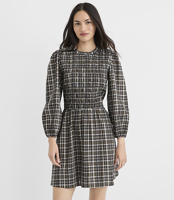 A woman in a plaid dress stands against a plain white background.