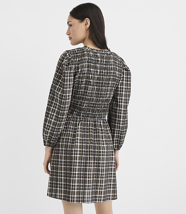 A woman in a plaid dress stands against a plain, light-colored background.