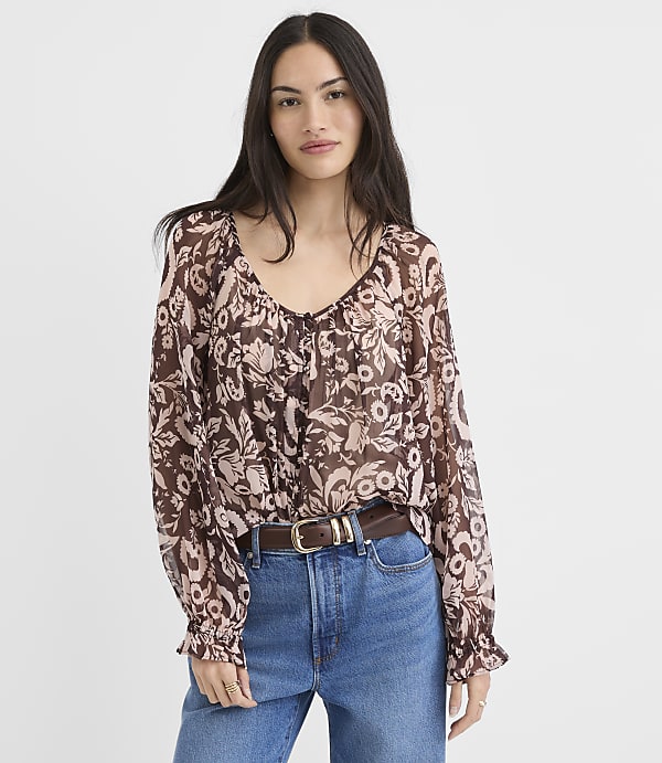 A woman in a floral print blouse and jeans stands against a plain white background.