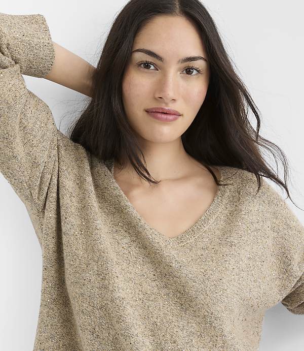 A woman with long dark hair and a v-neck sweater is in the foreground, with a plain white background.
