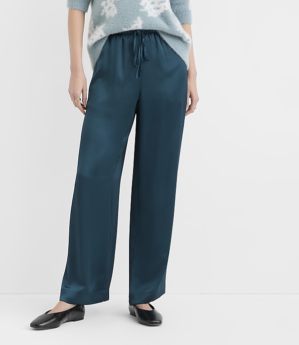 A person stands in teal satin pants and black flats against a plain white background.