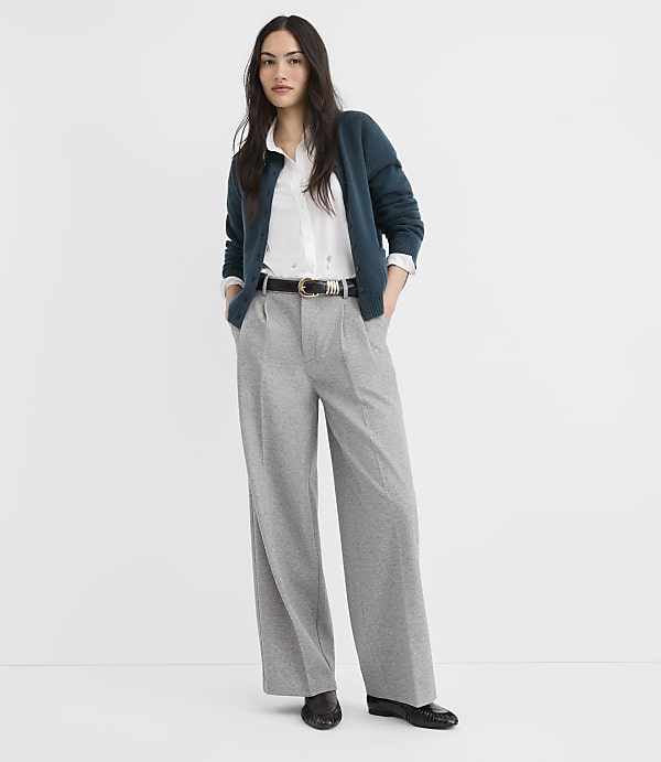 A woman in a teal cardigan and gray wide-leg pants stands against a plain white background.