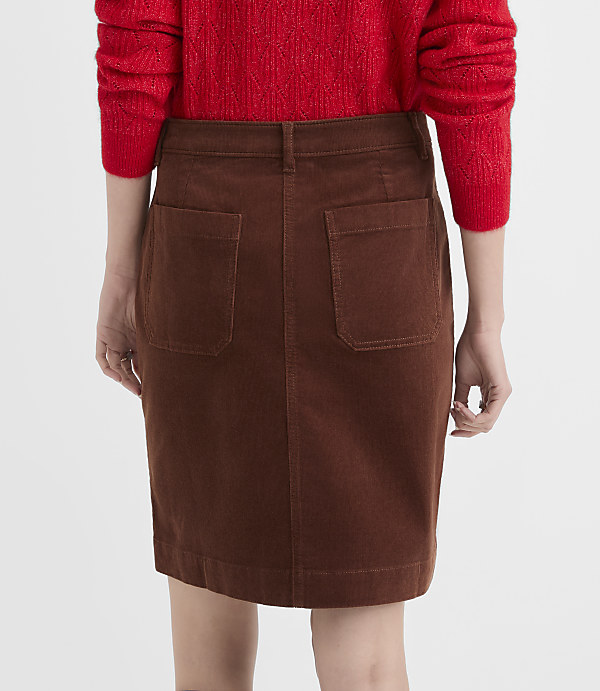 A person wearing a red sweater and a brown corduroy skirt stands against a plain white background.