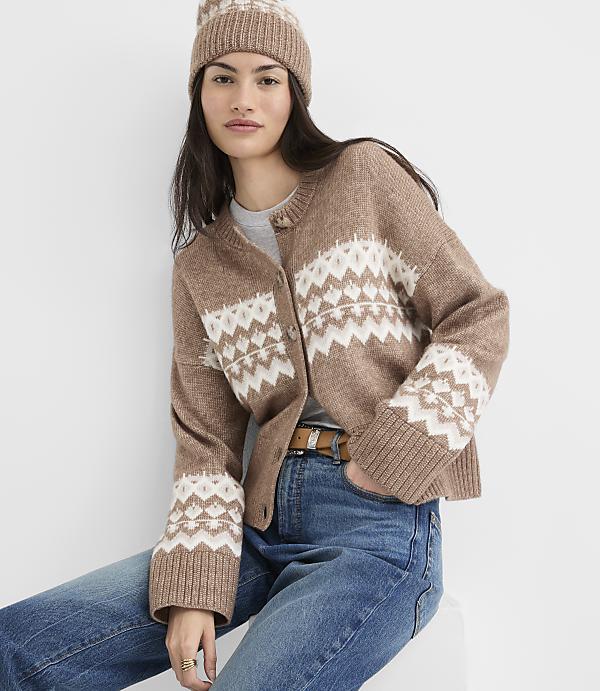 A woman in a brown fair isle cardigan and matching beanie poses in front of a plain white background.