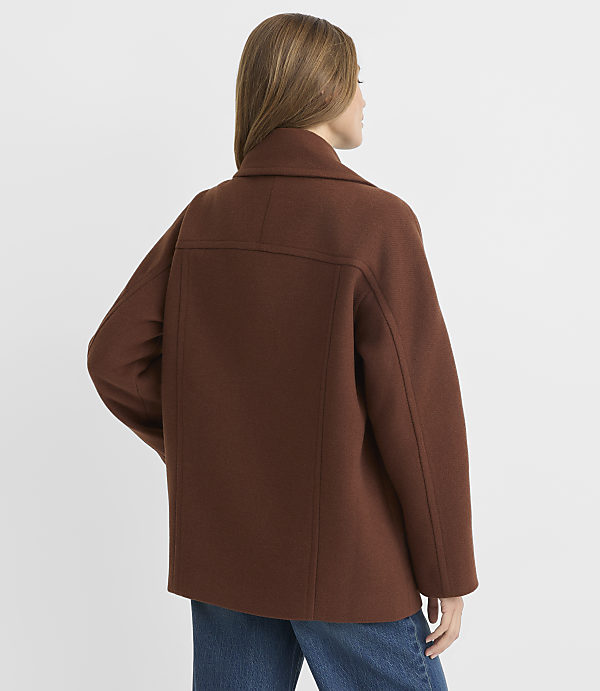 A woman in a brown jacket stands against a plain white background.