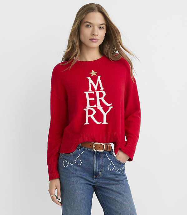 A woman in a red Christmas sweater and jeans stands against a plain white background.
