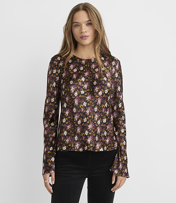A woman in a dark floral print blouse stands against a plain gray background.