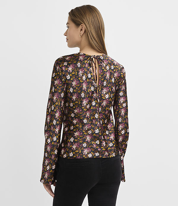 A woman in a floral print blouse with bell sleeves stands against a plain gray background.