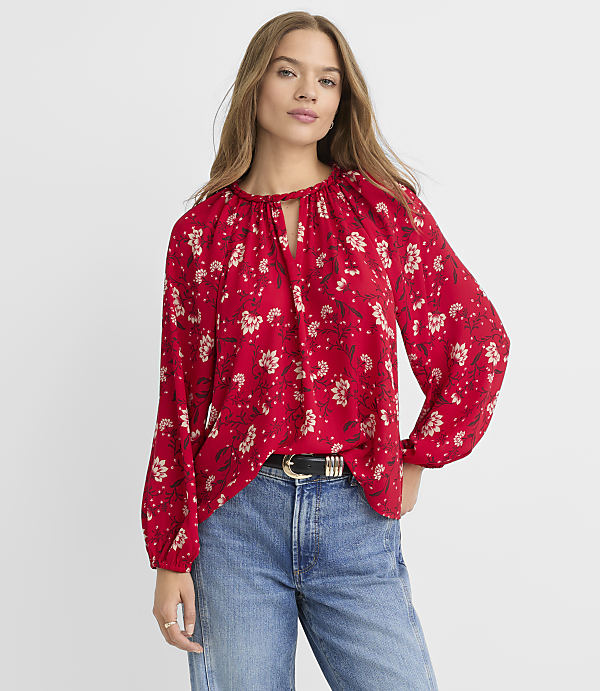 A woman in a red floral blouse and blue jeans stands against a plain white background.